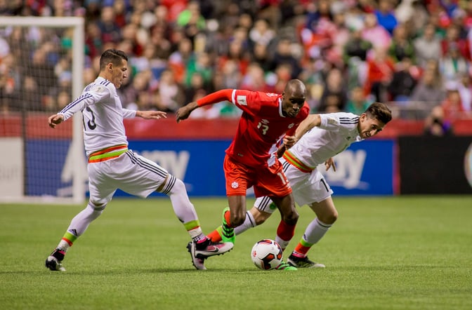 Atiba Hutchinson dribbling past defenders during an international soccer match for Canada.