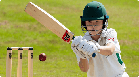Youth cricket player batting on a green field, representing Fusion Sports Park’s Phase 2A indoor prefab court facility for skill development.