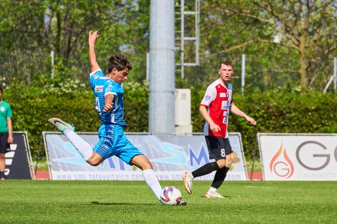 Youth soccer player taking a powerful shot during a competitive match, with defender in pursuit.