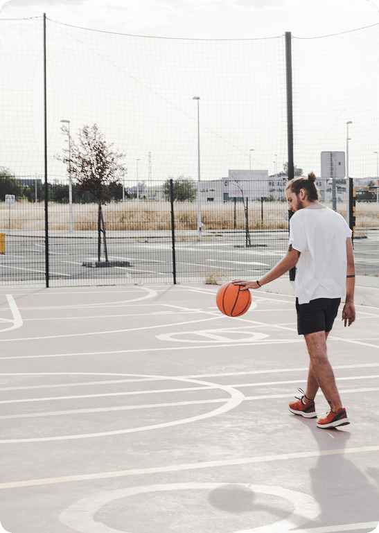 Man walking with a basketball on an empty outdoor court in an urban setting