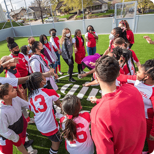 Diverse youth soccer team huddled together on a community mini-pitch, celebrating teamwork and local sports empowerment