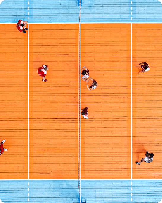 Aerial view of players on a bright orange hardcourt volleyball court with net, used for co-ed and women's recreational leagues.