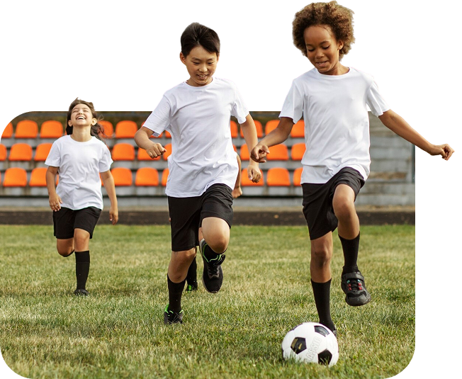 Three young kids playing 5v5 soccer on a grass field with stadium seating in the background
