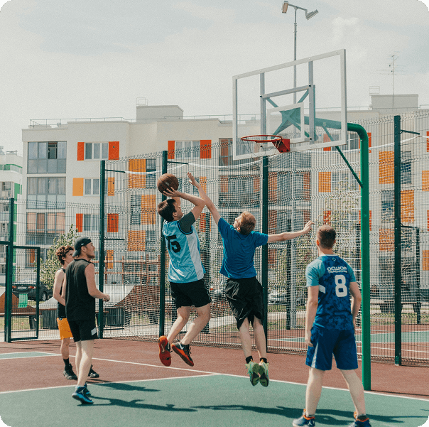 Group of players jumping for a rebound on an outdoor basketball court surrounded by city buildings
